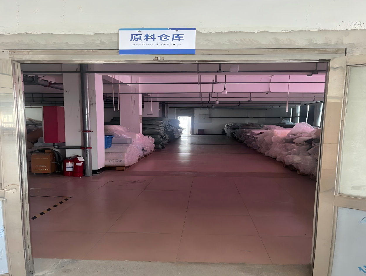 Raw material warehouse with a bilingual sign above the door and wrapped fabric rolls along both sides of the floor